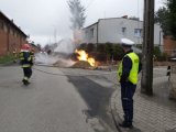 Na zdjęciu widać policjanta na drodze. W tle widać wykop, z którego wydobywają się płomienie. Ogień próbują ugasić strażacy.