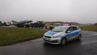 Na zdjęciu widać policyjny radiowóz z włączonymi sygnałami świetlnymi, za którym jadą inne pojazdy przewożące samolot wojskowy.