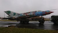 Na zdjęciu widać samolot wojskowy MIG-21 wieziony na przyczepie ciągniętej przez samochód ciężarowy.