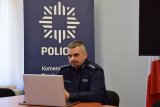 Na zdjęciu widać policyjnego profilaktyka, który siedzi przy biurku przed laptopem i prowadzi zajęcia z uczniami.