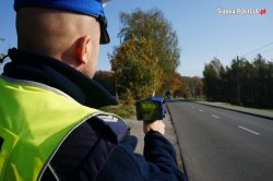 Na zdjęciu widać policjanta z drogówki patrzącego na drogę. W ręku trzyma urządzenia służące do pomiaru prędkości.