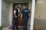 Na fotografii widać dwóch policjantów, którzy stoją przed wejściem do klatki schodowej bloku. Jeden z policjantów dzwoni na domofon.