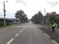 Na zdjęciu widać przejście dla pieszych w rejonie skrzyżowania. Po jednej stronie ulicy widać policyjny radiowóz, a po drugiej stronie policjanta.