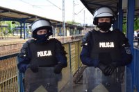 Na zdjęciu widać policjantów z oddziałów prewencji ubranych w hełmy i osłony. Policjanci stoją obok torowiska.