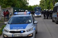 Na zdjęciu widać policyjne radiowozy, armatkę wodną oraz policjantów pilotujących idących drogą kibiców