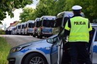 Na zdjęciu widać policjanta z drogówki stojącego przy radiowozie ustawionym w poprzek drogi. W tle widać policyjne radiowozy ustawione jeden za drugim.