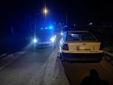 Na zdjęciu widać policyjne radiowozy z włączonymi sygnałami świetlnymi. Obok nich, na drodze widać samochód osobowy.