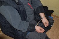 Na zdjęciu widać siedzącego na krześle mężczyznę, który ma ręce zapięte w kajdanki