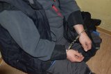 Na zdjęciu widać siedzącego na krześle mężczyznę, który ma ręce zapięte w kajdanki