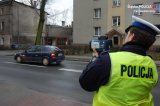 Na zdjęciu widać policjanta z drogówki patrzącego na drogę. W ręku trzyma urządzenia służące do pomiaru prędkości.
