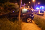 Na zdjęciu widać samochód osobowy zaparkowany w przydrożnym rowie. Obok samochodu widać policyjny radiowóz z włączonymi sygnałami świetlnymi.