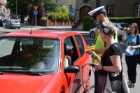 Na zdjęciu widać policjanta oraz dziennikarkę z radia, którzy rozmawiają z kierującą samochodu, zatrzymaną do kontroli drogowej.