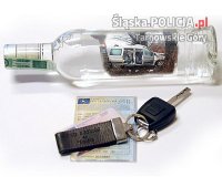 Zdjęcie przedstawia butelkę alkoholu, dowód rejestracyjny pojazdu oraz leżące na nim kluczyki do samochodu.
