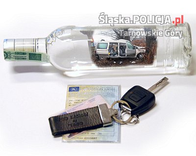 Zdjęcie przedstawia butelkę alkoholu, dowód rejestracyjny pojazdu oraz leżące na nim kluczyki do samochodu.