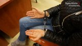 Na zdjęciu widać siedzącą na krześle kobietę, która ma zapięte ręce w kajdanki