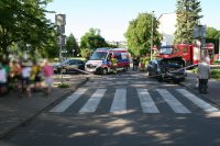 Na zdjęciu widać skrzyżowanie z przejściem dla pieszych, na którym znajdują się dwa rozbite samochody biorące udział w wypadku. Obok aut widać karetkę pogotowia, wozy strażackie i mieszkańców.