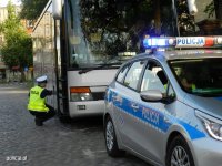 Na zdjęciu widać policjanta z drogówki, który sprawdza stan techniczny autobusu. Przed autokarem znajduje się policyjny radiowóz.