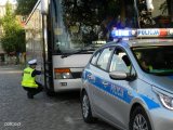 Na zdjęciu widać policjanta z drogówki, który sprawdza stan techniczny autobusu. Przed autokarem znajduje się policyjny radiowóz.