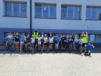 Na zdjęciu widać stojącą przed budynkiem szkoły grupę dzieci z rowerami. Wśród nich widać policjantów.
