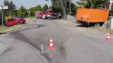 Na zdjęciu widać skrzyżowanie, na którym w przydrożnym rowie leży samochód fiat, po drugiej stronie ulicy samochód iveco wbity w ogrodzenie posesji. W tle zdjęcia widać policyjny radiowóz i policjanta oraz wozy strażackie.