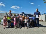 Na zdjęciu widać policjanta, który stoi obok grupy dzieci. Policjant trzyma w ręku dyplom z podziękowaniem