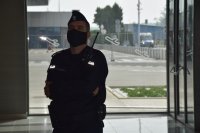Na zdjęciu widać policjanta stojącego wewnątrz budynku. W tle przez szybę widać policyjny radiowóz.