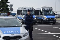 Na zdjęciu widać policjanta stojącego obok radiowozów znajdujących się na parkingu lotniska.