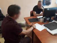 Na zdjęciu widać siedzących przy biurku: policjanta, który przesłuchuje zatrzymanego mężczyznę