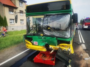 Na zdjęciu widać przód autobusu miejskiego. Pojazd jest uszkodzony-ma zgnieciony i połamany zderzak oraz spękaną przednią szybę.