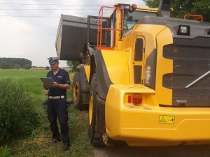 Na zdjęciu widać  policjanta z drogówki stojącego obok ładowarki. Mundurowy trzyma w ręce notatki.