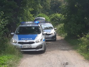 Na zdjęciu widać policyjne radiowozy zaparkowane na polnej drodze.