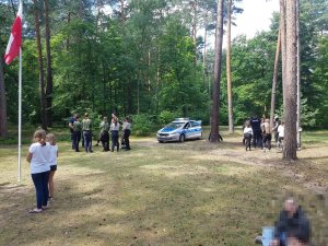 Na zdjęciu widać policjantów rozmawiających z harcerzami i policyjny radiowóz zaparkowany przy obozowisku.