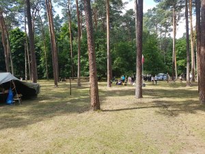 Na zdjęciu widać namiot rozbity wśród drzew. W tle zdjęcia widać grupę młodzieży rozmawiającą z policjantami.