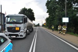 Na zdjęciu widać samochód ciężarowy-cysternę, przed którym stoi policyjny radiowóz. Na chodniku stoją policjanci i strażacy.