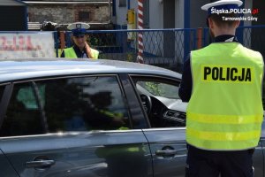 Na zdjęciu widać policjantkę i policjanta kontrolujących kierowcę samochodu zatrzymanego do kontroli drogowej.