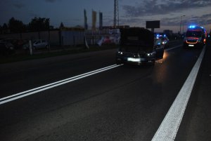 Na zdjęciu widać: na środku drogi samochód osobowy marki volkswagen z podniesioną do góry maską. Za samochodem widać karetkę pogotowia oraz policyjny radiowóz z włączonymi sygnałami świetlnymi.