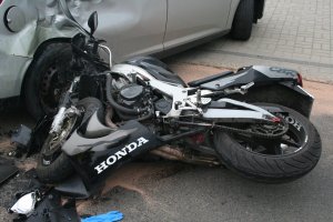 Na zdjęciu widać motocykl leżący na drodze i samochód osobowy, w który wjechał motocyklista.