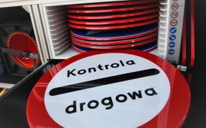 Zdjęcie kolorowe. Widoczny okrągły znak biało-czerwony. W środku znaku napis kontrola drogowa