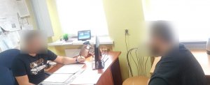 wnętrze pokoju w komisariacie, podczas czynności z zatrzymanym. zdjecie przedstawia dwóch mężczyzn z zamazanymi twarzami