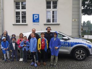 Policjant w towarzystowie młodzieży na tle komisariatu i oznakowanego radiowozu