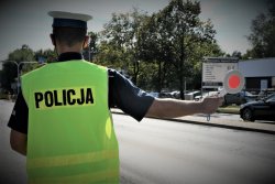 Na zdjęciu widać policjanta z drogówki stojącego przy drodze i trzymającego w ręku &quot;lizak&quot; - tarczę służącą do zatrzymywania pojazdów.