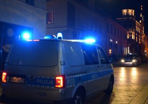 Na zdjęciu widać dwa policyjne radiowozy z włączonymi sygnałami świetlnymi.