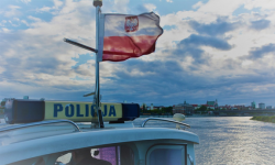 Na zdjęciu widać dach łodzi motorowej znajdującej się na rzece. Na dachu widać policyjny kogut z napisem Policja oraz powiewającą na wietrze biało-czerwoną flagę.
