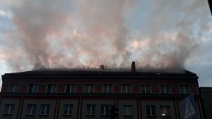 Na zdjęciu widać kamienicę. Z jej dachu wydobywa się gęsty dym.