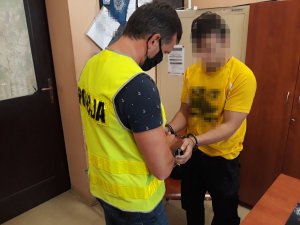 Na zdjęciu widać policjanta, który zakłada zatrzymanemu mężczyźnie kajdanki na ręce wyciągnięte do przodu.
