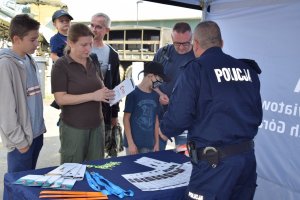 Na zdjęciu widać policjanta oraz grupę rodziców z dziećmi stojących przed policyjnym profilaktycznym namiotem.