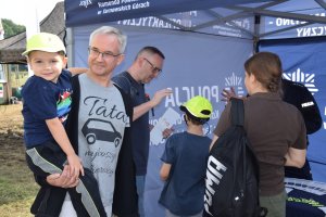 Na zdjęciu widać grupę rodziców z dziećmi, które mają na głowach czapki z daszkiem promujące kampanię społeczną „Mamo! Tato! Tutaj jestem”.