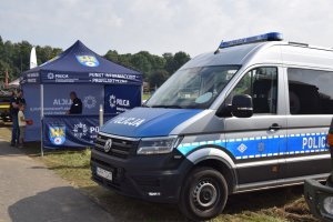 Na zdjęciu widać policyjny radiowóz oraz policyjny namiot profilaktyczny, pod którym stoi policjant.