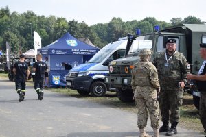 Na zdjęciu widać żołnierzy, strażaków, wozy wojskowe, policyjny radiowóz oraz policyjny namiot profilaktyczny.