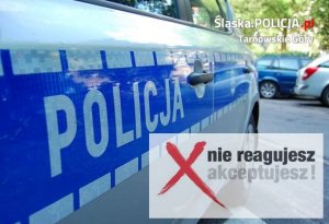 Na zdjęciu widać bok policyjnego radiowozu, na którym znajduje się napis POLICJA. z prawej strony zdjęcia czerwony znak X i napis: Nie reagujesz -akceptujesz.
